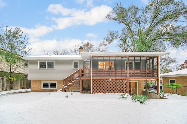 snow covered rear of property with a sunroom