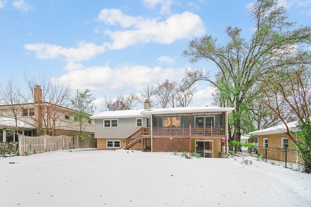 snow covered rear of property with a sunroom