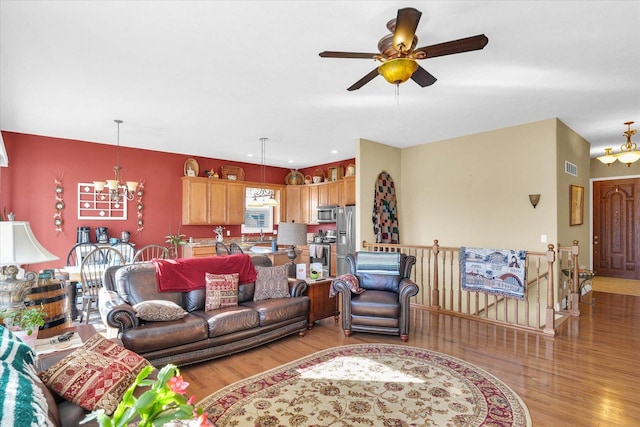 living room with visible vents, light wood-style flooring, and ceiling fan with notable chandelier