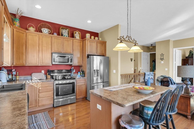 kitchen with a sink, a kitchen breakfast bar, a center island, stainless steel appliances, and light wood-style floors