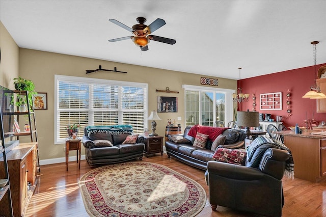 living room with baseboards, wood finished floors, and ceiling fan with notable chandelier