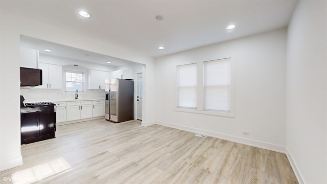 kitchen with sink, backsplash, light hardwood / wood-style floors, white cabinets, and black appliances