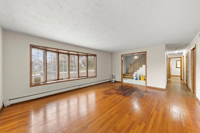 empty room with wood-type flooring, a textured ceiling, and baseboard heating