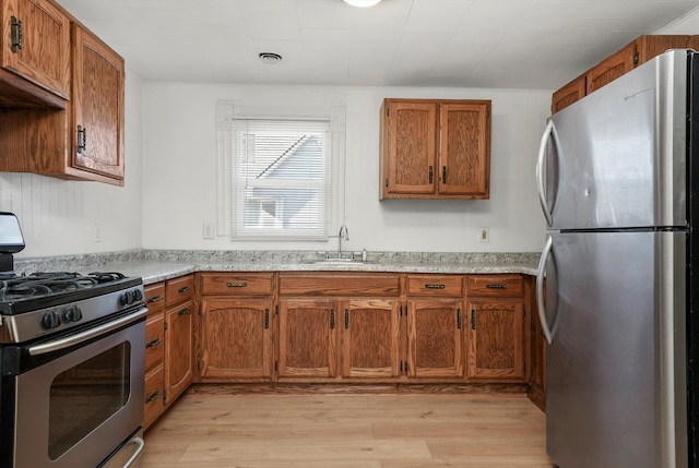 kitchen featuring sink, light stone countertops, stainless steel appliances, and light hardwood / wood-style flooring