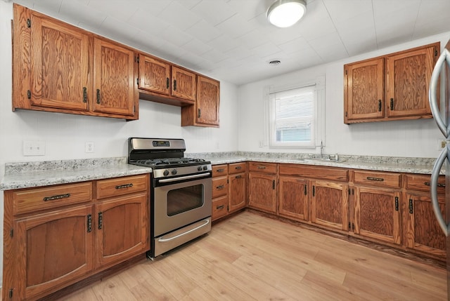 kitchen with light hardwood / wood-style floors, light stone countertops, stainless steel range with gas cooktop, and sink