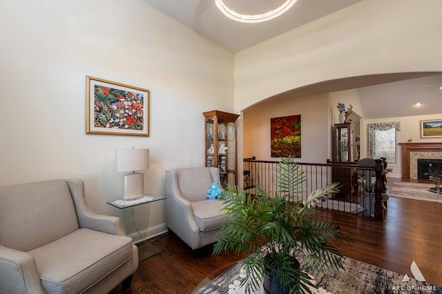 sitting room with a stone fireplace, dark wood-type flooring, and lofted ceiling