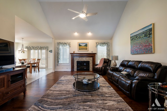 living room with ceiling fan with notable chandelier, dark hardwood / wood-style floors, a stone fireplace, and high vaulted ceiling