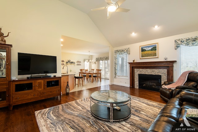 living room featuring a stone fireplace, dark hardwood / wood-style flooring, high vaulted ceiling, and ceiling fan with notable chandelier