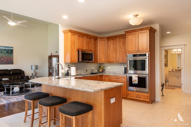 kitchen with sink, light hardwood / wood-style flooring, light stone countertops, kitchen peninsula, and stainless steel appliances