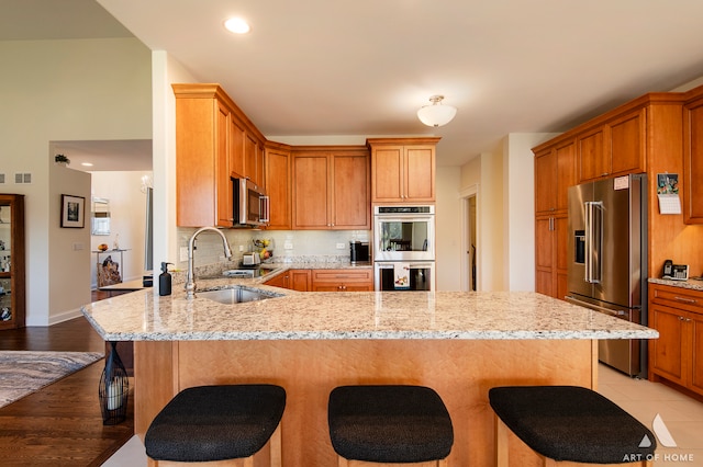 kitchen with sink, a breakfast bar area, light stone countertops, light wood-type flooring, and stainless steel appliances