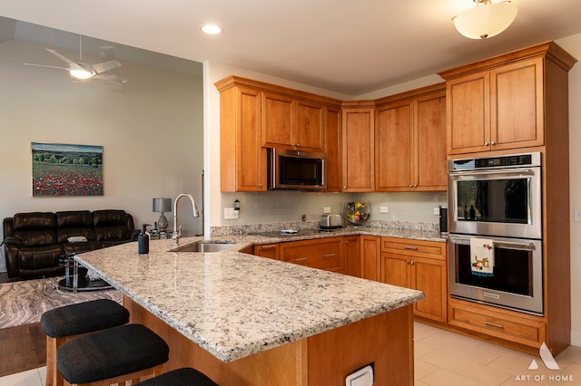 kitchen featuring sink, appliances with stainless steel finishes, tasteful backsplash, kitchen peninsula, and a breakfast bar area