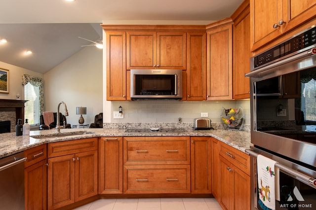 kitchen with sink, light stone counters, vaulted ceiling, decorative backsplash, and appliances with stainless steel finishes