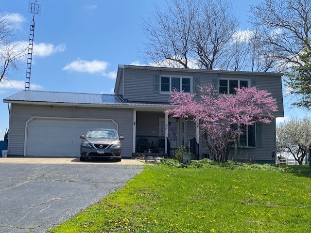 1522 E 7th Rd, Lostant, IL 61334 - traditional home featuring a porch, a front lawn, metal roof, aphalt driveway, and an attached garage