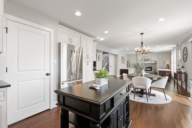 kitchen with a center island, dark wood-type flooring, stainless steel fridge, a fireplace, and white cabinets