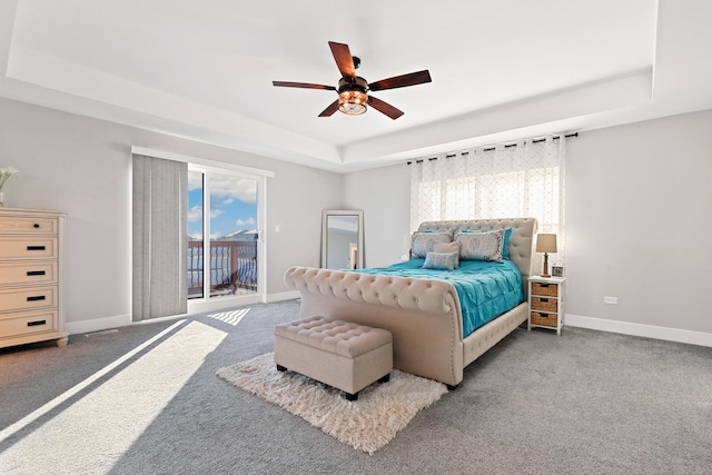 carpeted bedroom featuring a tray ceiling, multiple windows, and ceiling fan