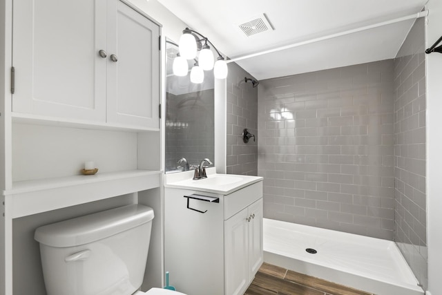 bathroom with tiled shower, toilet, vanity, and hardwood / wood-style flooring