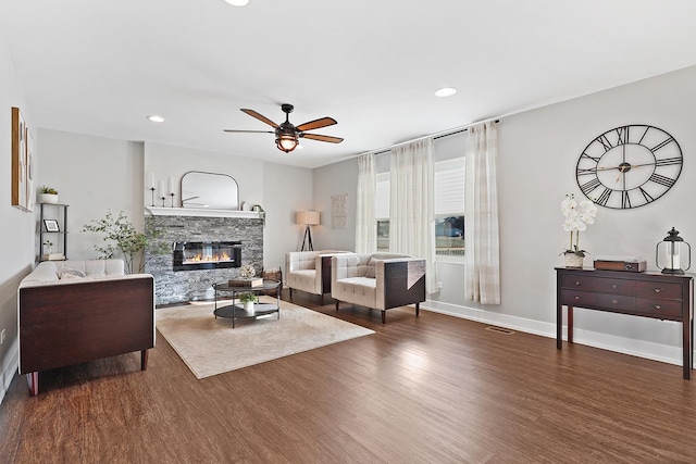 living room with dark hardwood / wood-style flooring, a stone fireplace, and ceiling fan