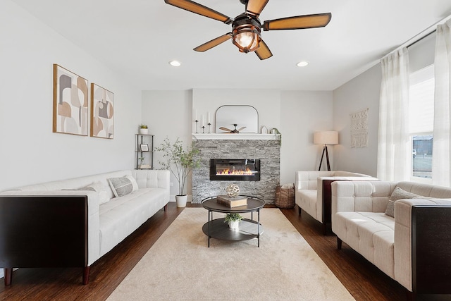 living room featuring dark hardwood / wood-style flooring, a stone fireplace, and ceiling fan