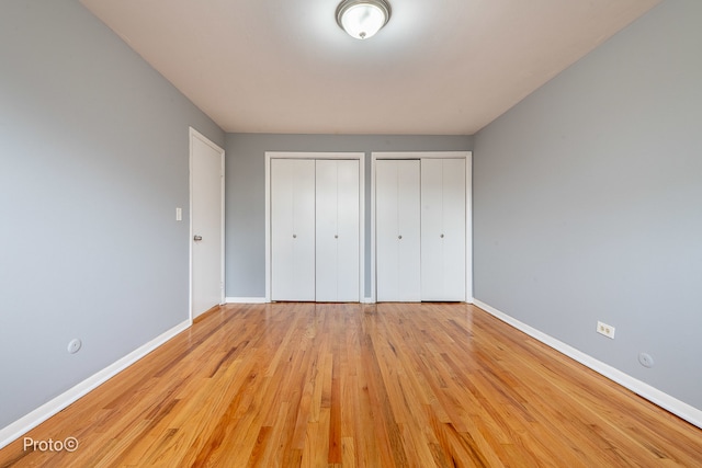 unfurnished bedroom featuring light hardwood / wood-style floors and multiple closets