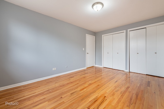 unfurnished bedroom with light hardwood / wood-style flooring and two closets