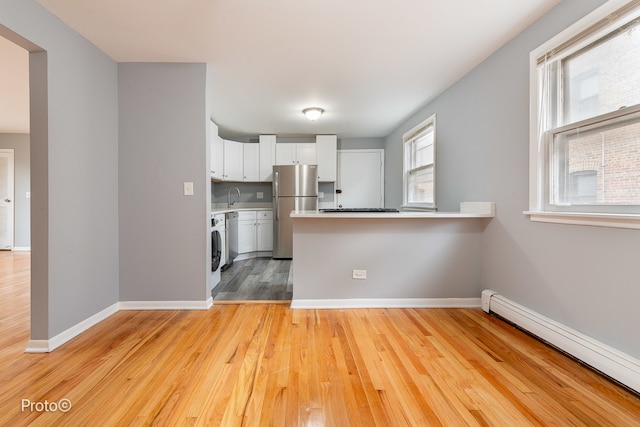 kitchen featuring white cabinets, a baseboard radiator, light hardwood / wood-style floors, kitchen peninsula, and stainless steel refrigerator