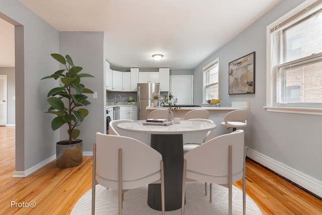 dining room with a baseboard heating unit, sink, and light hardwood / wood-style flooring