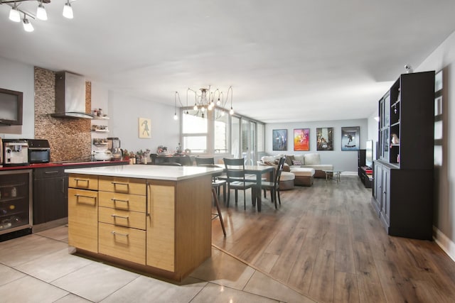 kitchen with a center island, wine cooler, wall chimney exhaust hood, light wood-type flooring, and a chandelier