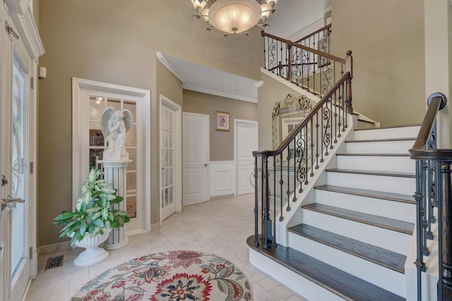 tiled foyer with a notable chandelier, a towering ceiling, and crown molding