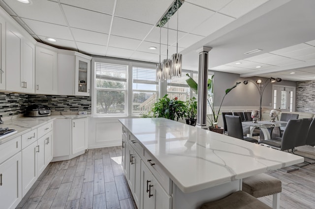 kitchen with a paneled ceiling, a center island, a kitchen bar, and white cabinets