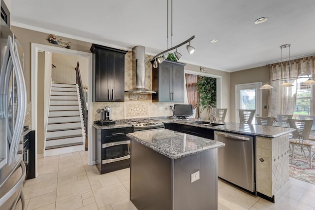 kitchen with a center island, sink, hanging light fixtures, stainless steel appliances, and wall chimney range hood