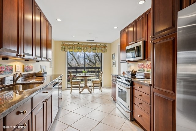 kitchen featuring dark stone counters, sink, light tile patterned floors, and stainless steel appliances