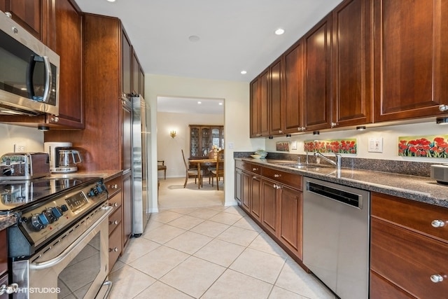 kitchen featuring dark stone countertops, sink, light tile patterned floors, and stainless steel appliances