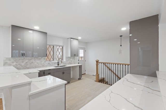 kitchen with gray cabinetry, pendant lighting, sink, decorative backsplash, and light stone counters