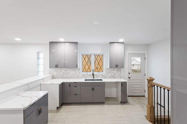 kitchen with backsplash, sink, gray cabinets, light stone countertops, and kitchen peninsula