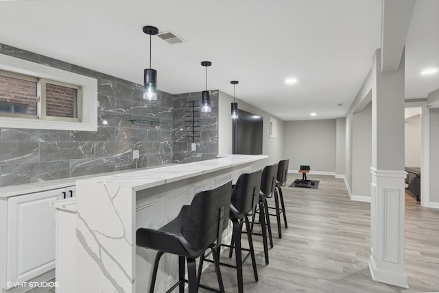 bar with light stone countertops, light wood-type flooring, tasteful backsplash, decorative light fixtures, and white cabinetry