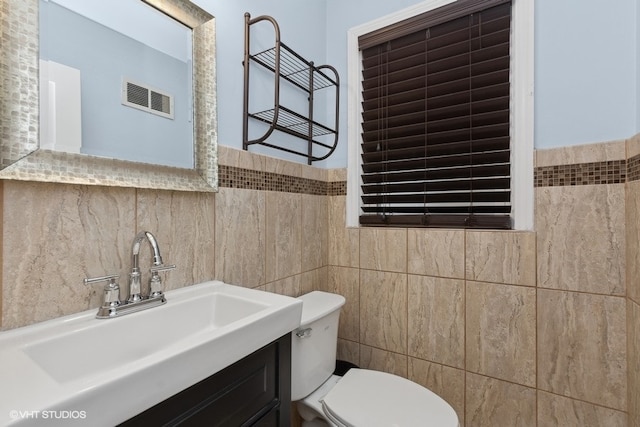 bathroom featuring vanity, toilet, and tile walls