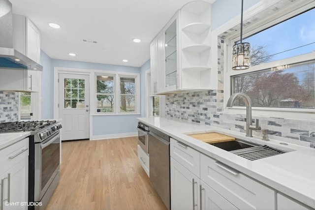 kitchen featuring white cabinetry, wall chimney range hood, decorative light fixtures, decorative backsplash, and appliances with stainless steel finishes