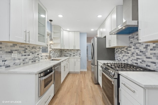 kitchen with wall chimney exhaust hood, light hardwood / wood-style flooring, backsplash, white cabinets, and appliances with stainless steel finishes