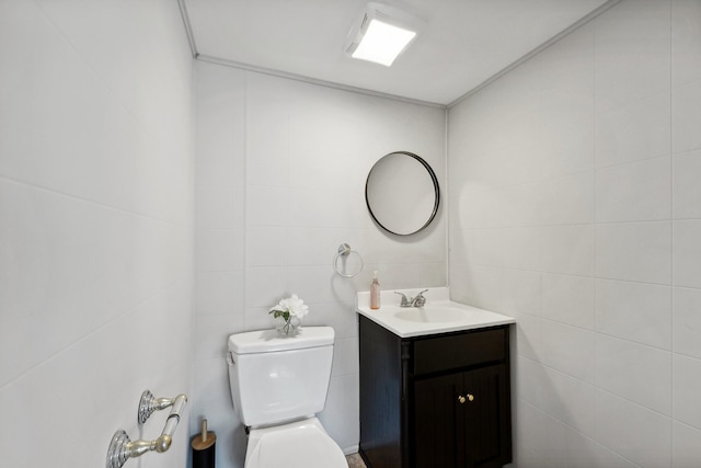 bathroom featuring vanity, toilet, and tile walls