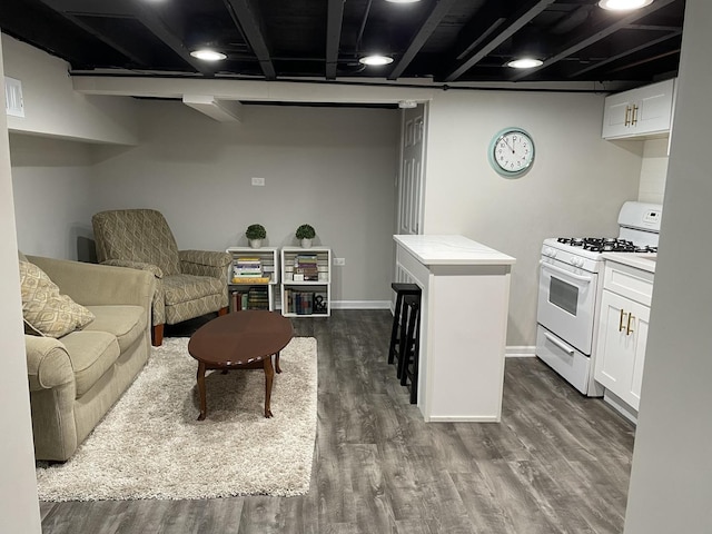 kitchen with white gas range, tile counters, a kitchen breakfast bar, dark hardwood / wood-style floors, and white cabinets