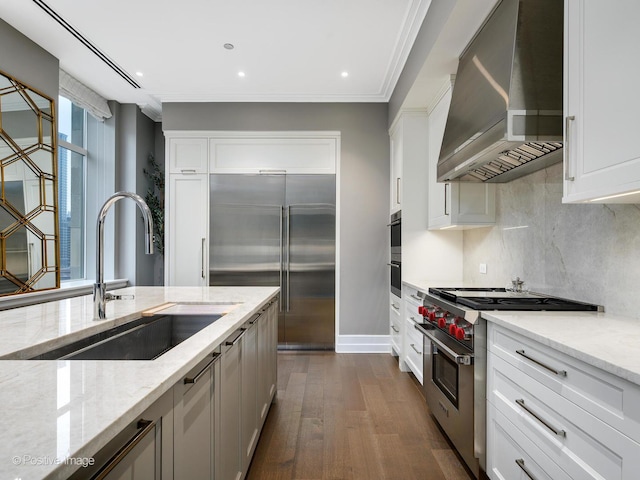 kitchen featuring white cabinetry, sink, high end appliances, light stone countertops, and wall chimney range hood