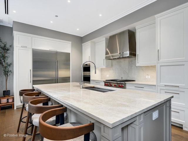 kitchen featuring wall chimney exhaust hood, sink, a kitchen island with sink, and white cabinets