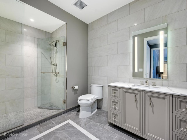 bathroom featuring a shower with door, vanity, tile walls, and toilet