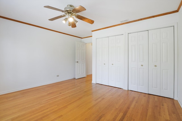 unfurnished bedroom featuring multiple closets, ceiling fan, light hardwood / wood-style flooring, and crown molding