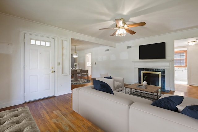 living room with hardwood / wood-style flooring, ceiling fan, ornamental molding, and a tiled fireplace