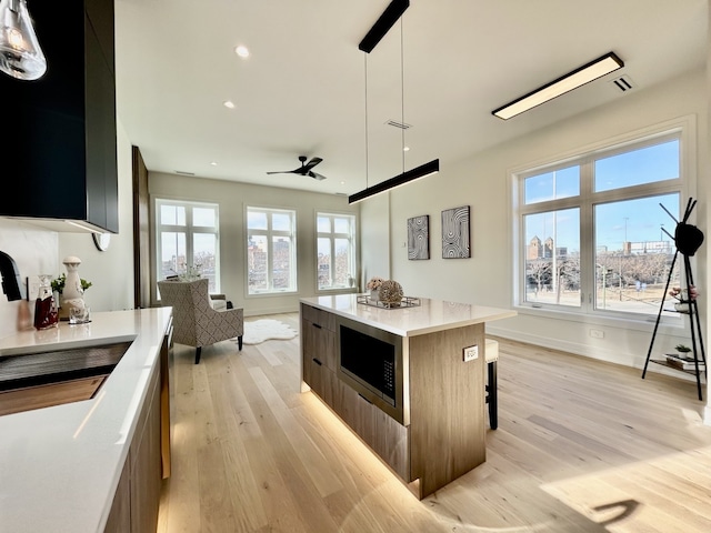 kitchen featuring hanging light fixtures, light hardwood / wood-style flooring, stainless steel microwave, a kitchen island, and a wealth of natural light