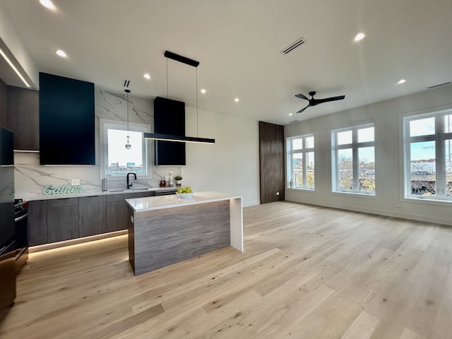 kitchen with a kitchen island, pendant lighting, decorative backsplash, ceiling fan, and light hardwood / wood-style floors