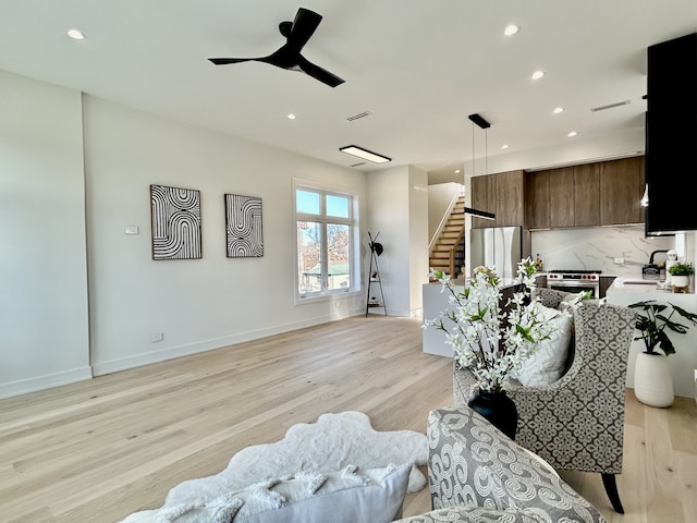 living room featuring ceiling fan, sink, and light wood-type flooring