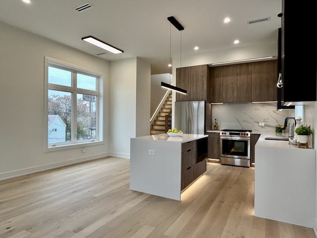 kitchen with sink, light hardwood / wood-style flooring, appliances with stainless steel finishes, a center island, and decorative light fixtures