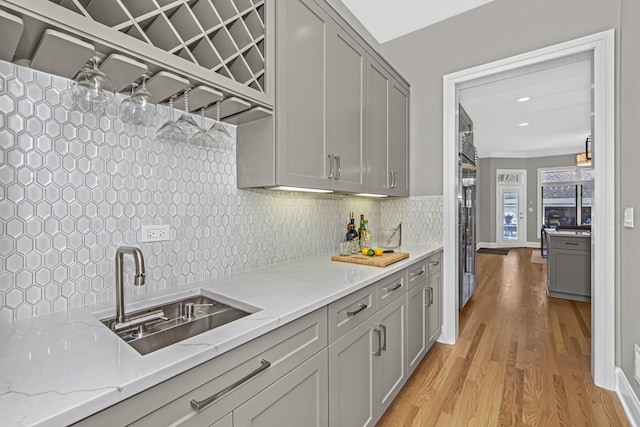 kitchen with sink, light hardwood / wood-style flooring, gray cabinets, light stone countertops, and backsplash